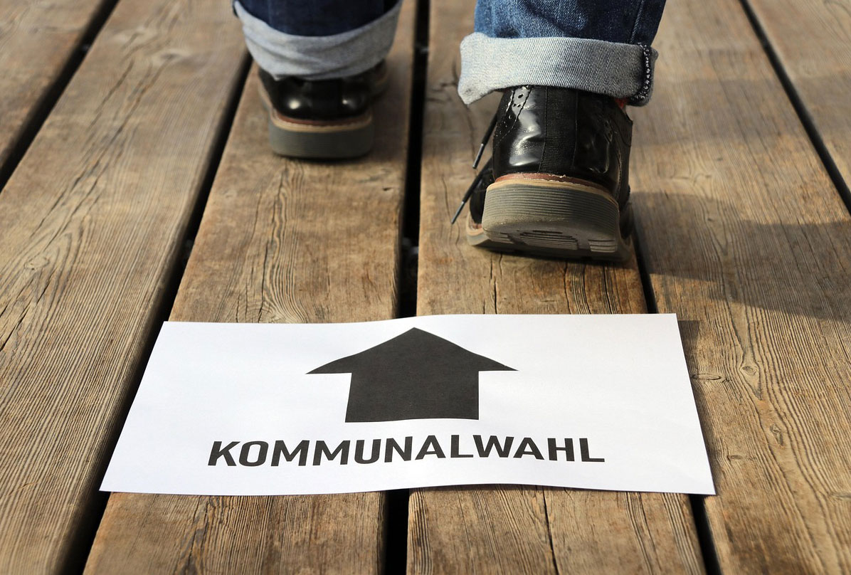 Papierschild Kommunalwahl mit Richtungspffleil leigt am Holzboden