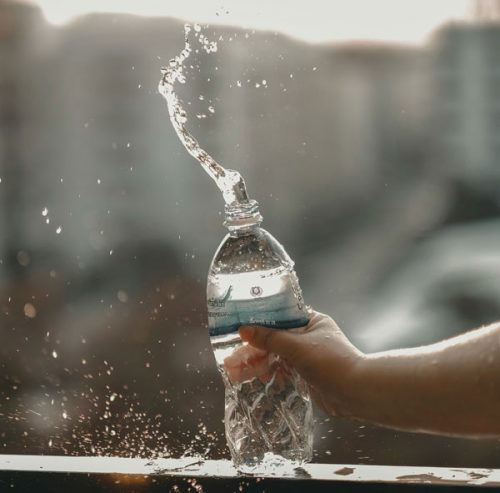 Hand knallt spritzende Wasserflasche auf ein Geländer